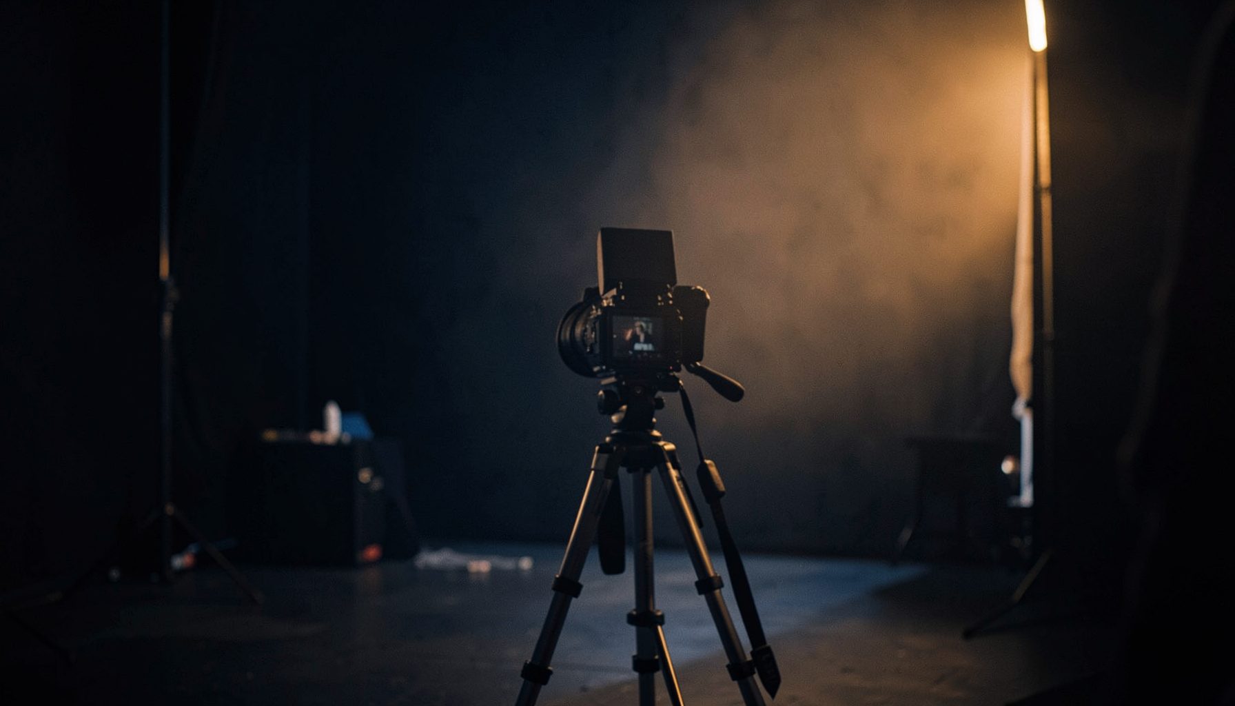 Softly lit film set with a camera on a tripod facing an off-screen subject, warm amber and deep navy tones, cinematic mood